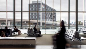 Un moderno terminal aeroportuario con grandes ventanales, una zona de descanso y un edificio con un letrero al fondo.