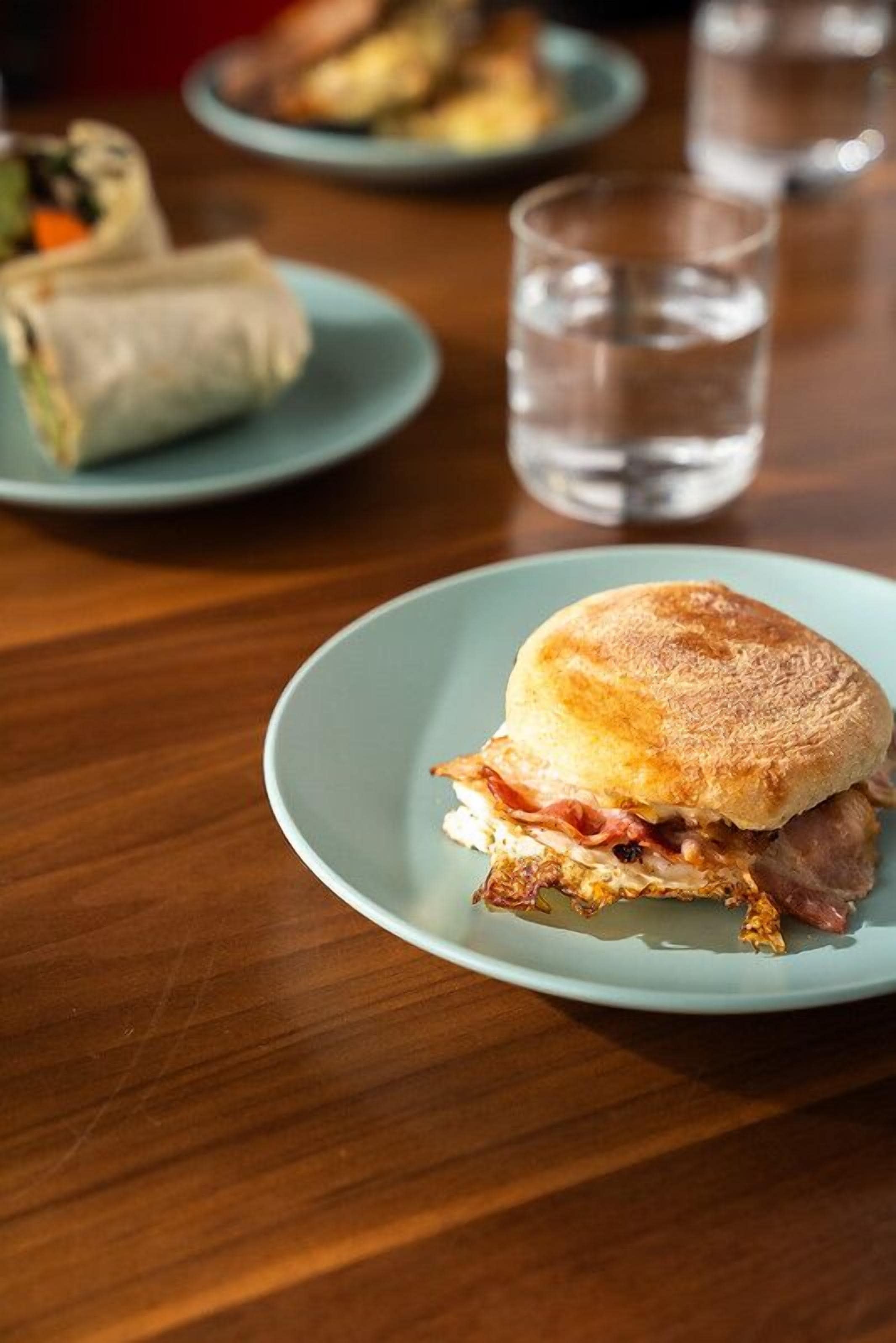 Un sándwich en un plato con un vaso de agua y otro plato con un wrap al fondo.