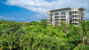 Ein modernes Mehrstöckiges Hotel mit Balkonen, umgeben von üppiger Vegetation und Blick auf den Ozean.