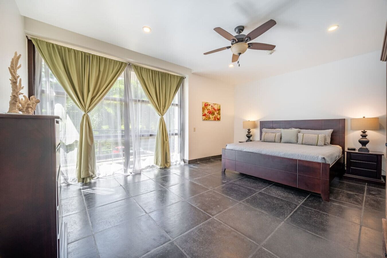 A bedroom with a bed, a ceiling fan, a nightstand, and a window with curtains.