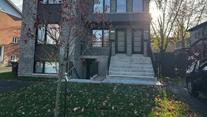 Une maison moderne à deux étages, avec une façade en briques, de grandes fenêtres et un numéro de maison bien visible.