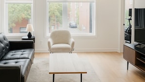 Un salon moderne avec un canapé en cuir noir, un fauteuil blanc, une table basse en bois et un meuble pour la télévision.