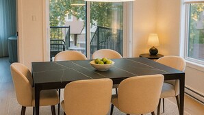 Un coin repas avec une table noire, des chaises beiges, un saladier de fruits et une suspension.