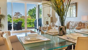 A dining area with a glass table, white plates, and wine glasses. There is a vase with flowers on the table. - Tamarindo Diria 403 Luxury Ocean View Condo (Tamarindo)