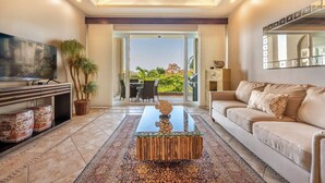 A modern living room with a TV, a sofa, a coffee table, and a view of the outdoors. - Tamarindo Diria 403 Luxury Ocean View Condo (Tamarindo)