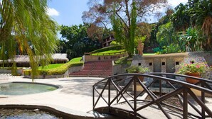 A bridge over a water feature, surrounded by lush greenery and a stone structure with steps leading up to a building labeled "L. DIRIA". - Tamarindo Diria 403 Luxury Ocean View Condo (Tamarindo)