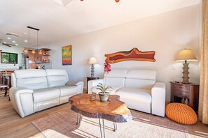 A living room with two white sofas, a wooden coffee table, and a dining area in the background.