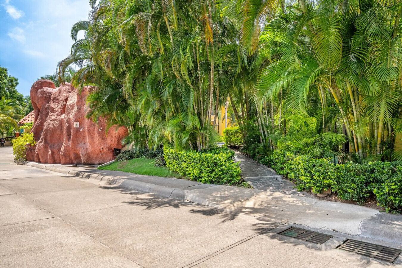 A paved pathway flanked by lush greenery and a prominent rock formation.
