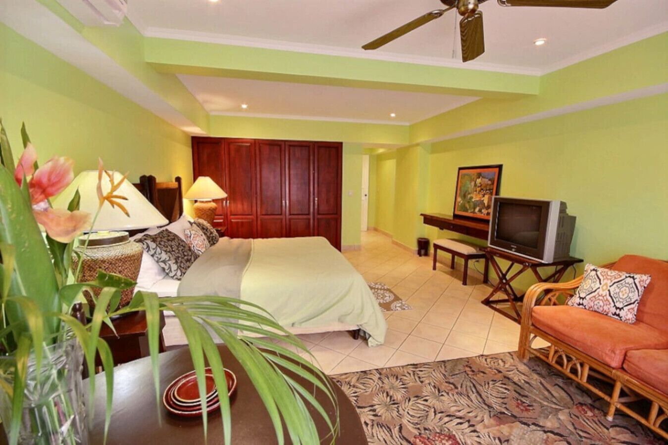 Ein Hotelzimmer mit einem Bett, einem Fernseher, einer Couch und einem Esstisch mit einer Blumenvase.