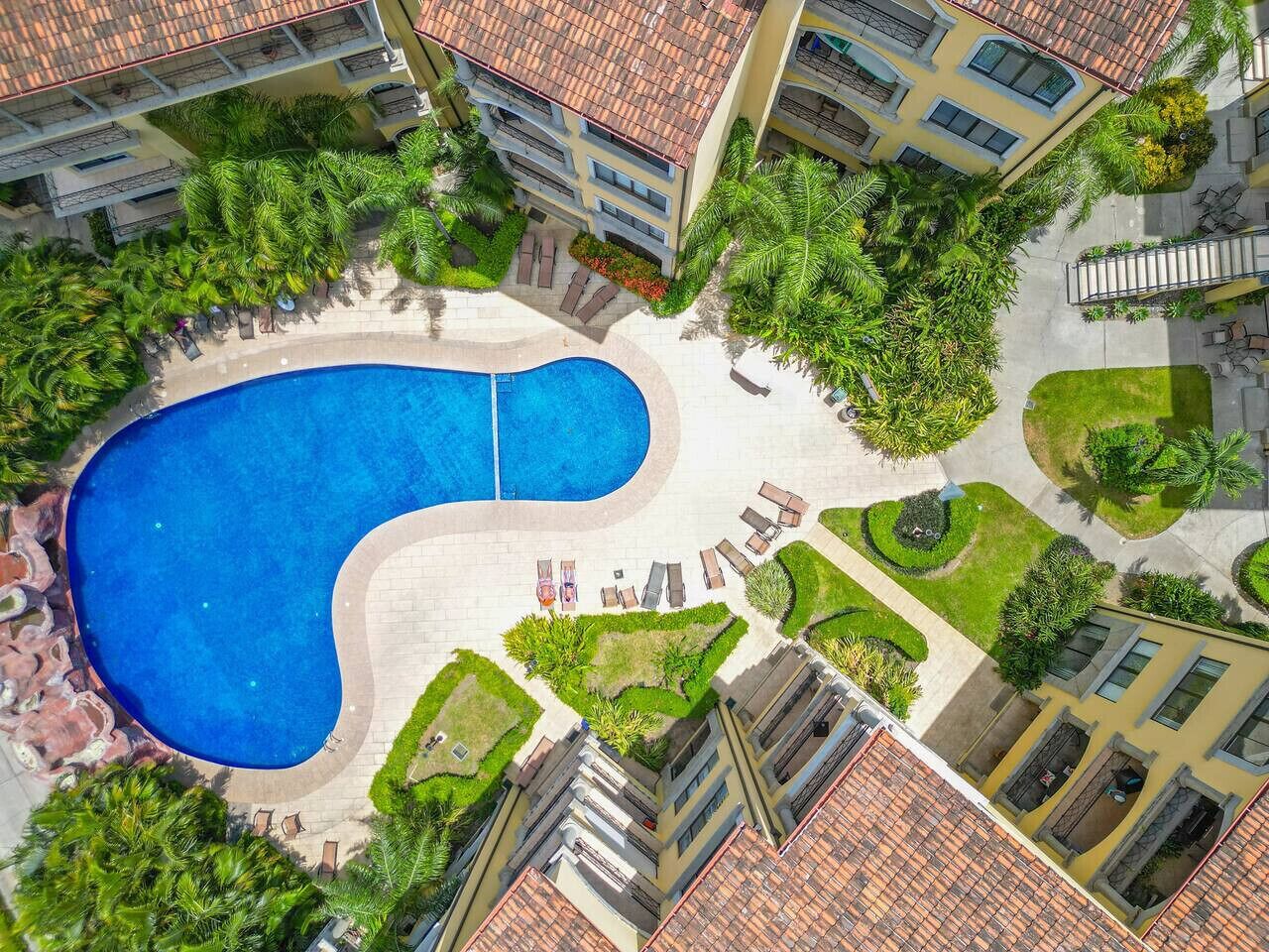 Vista aérea de un hotel con una amplia piscina, múltiples balcones y un exuberante paisaje.