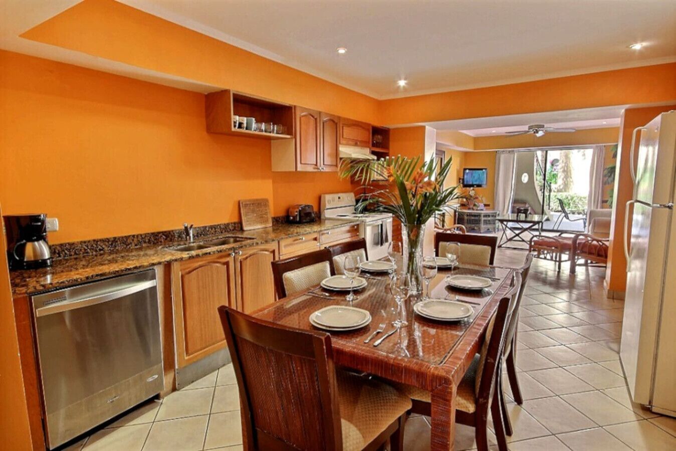 A modern kitchen with a dining area, featuring a granite countertop, stainless steel appliances, and a wooden dining table set for six.