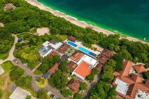 Vista aèria d'un complex turístic a la costa, amb piscina, accés a la platja i vegetació exuberant.