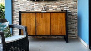 A room with a stone wall, a wooden cabinet, and a wicker chair. - Villa Sol y Mar Shared Pool 2 miles to Beach (Potrero)