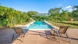 A rectangular swimming pool with clear blue water, surrounded by a wooden deck and two lounge chairs. - Villa Sol y Mar Shared Pool 2 miles to Beach (Potrero)
