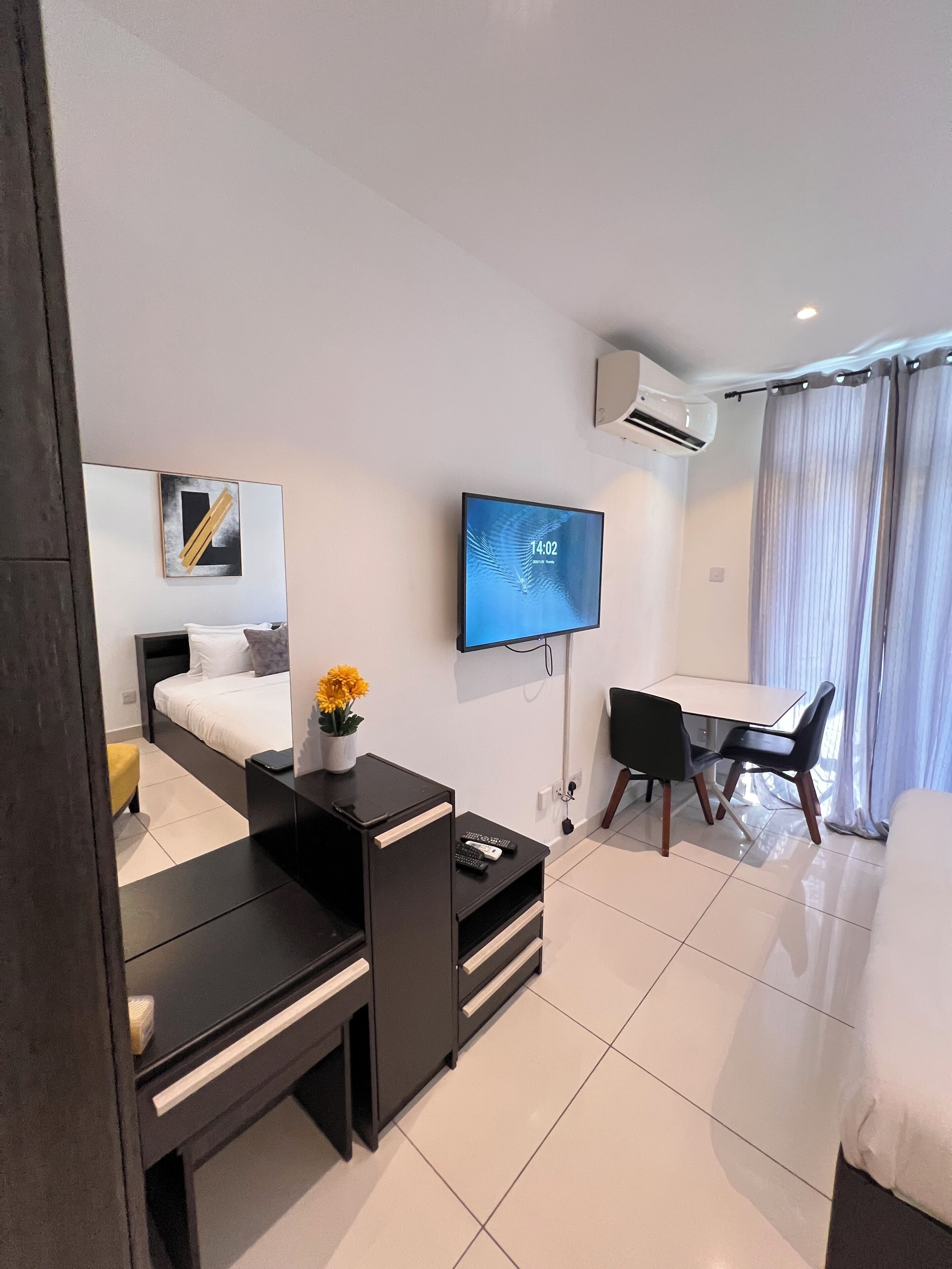 A modern hotel room with a bed, a desk, a chair, a TV, and an air conditioning unit.