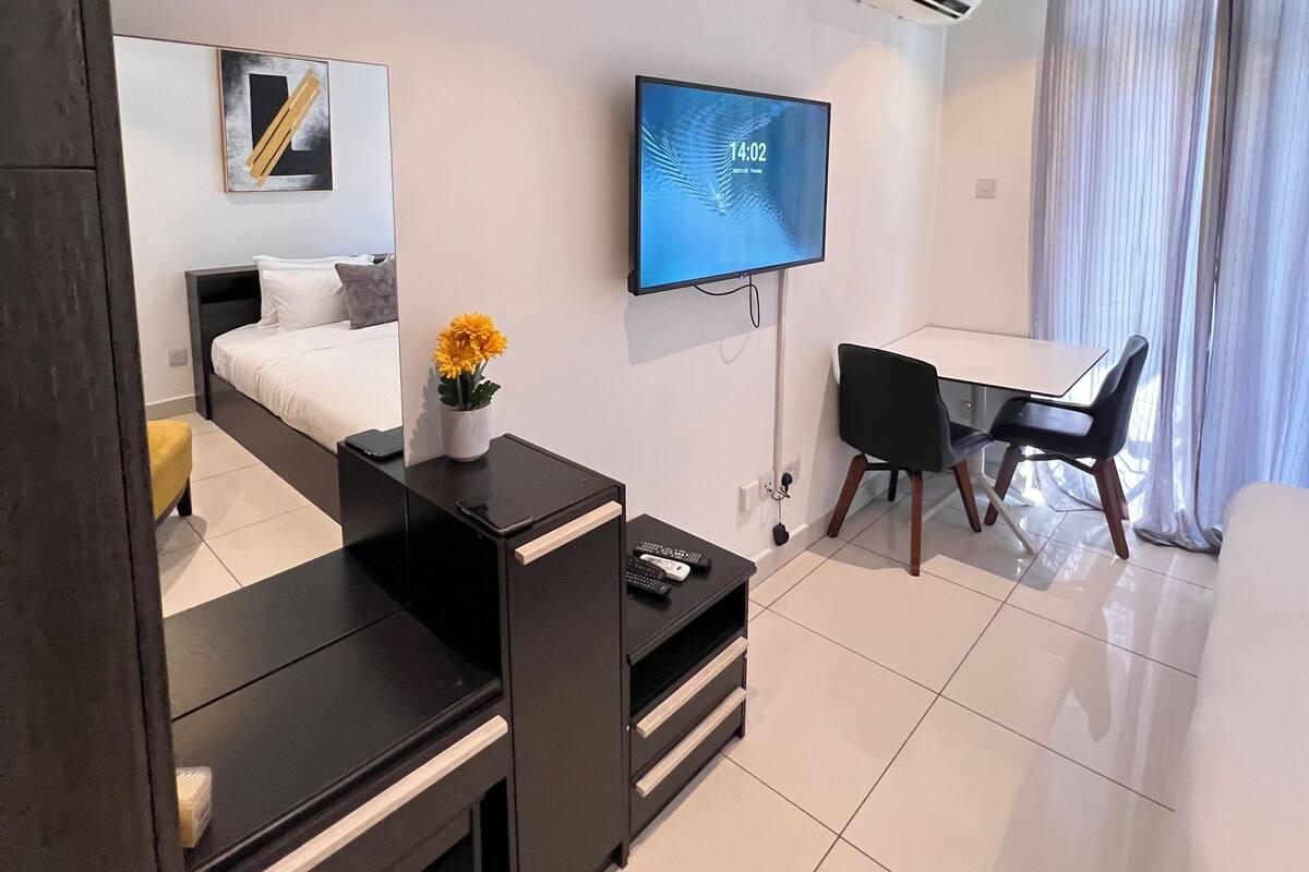 Una habitación de hotel moderna con cama, escritorio, silla, televisor y aire acondicionado.