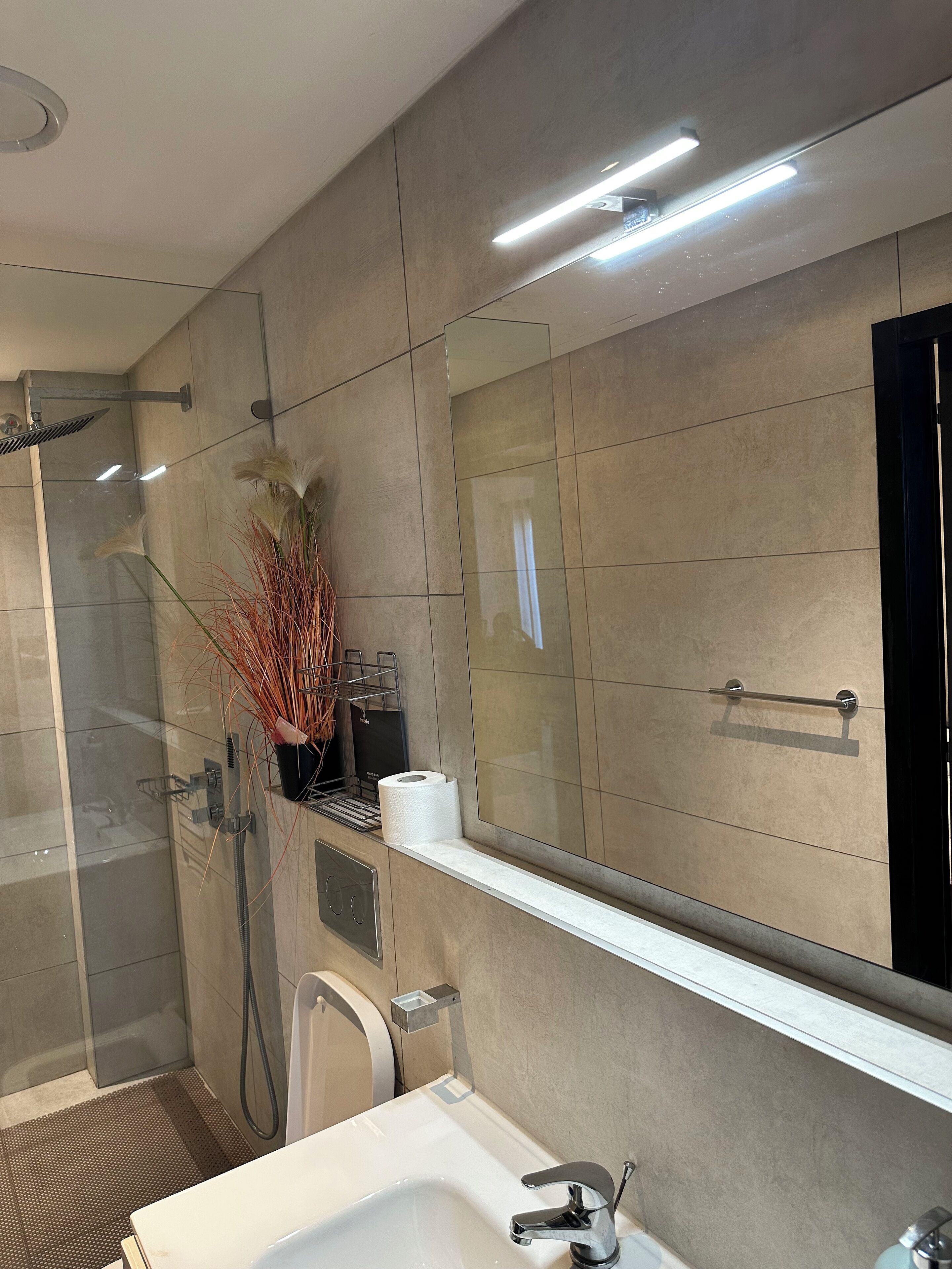 Une salle de bain moderne avec un grand miroir, une douche et un lavabo.