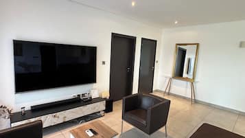 A modern living room with a flat-screen TV, a marble console, a coffee table, a brown sofa, a leather armchair, and a mirror on the wall.