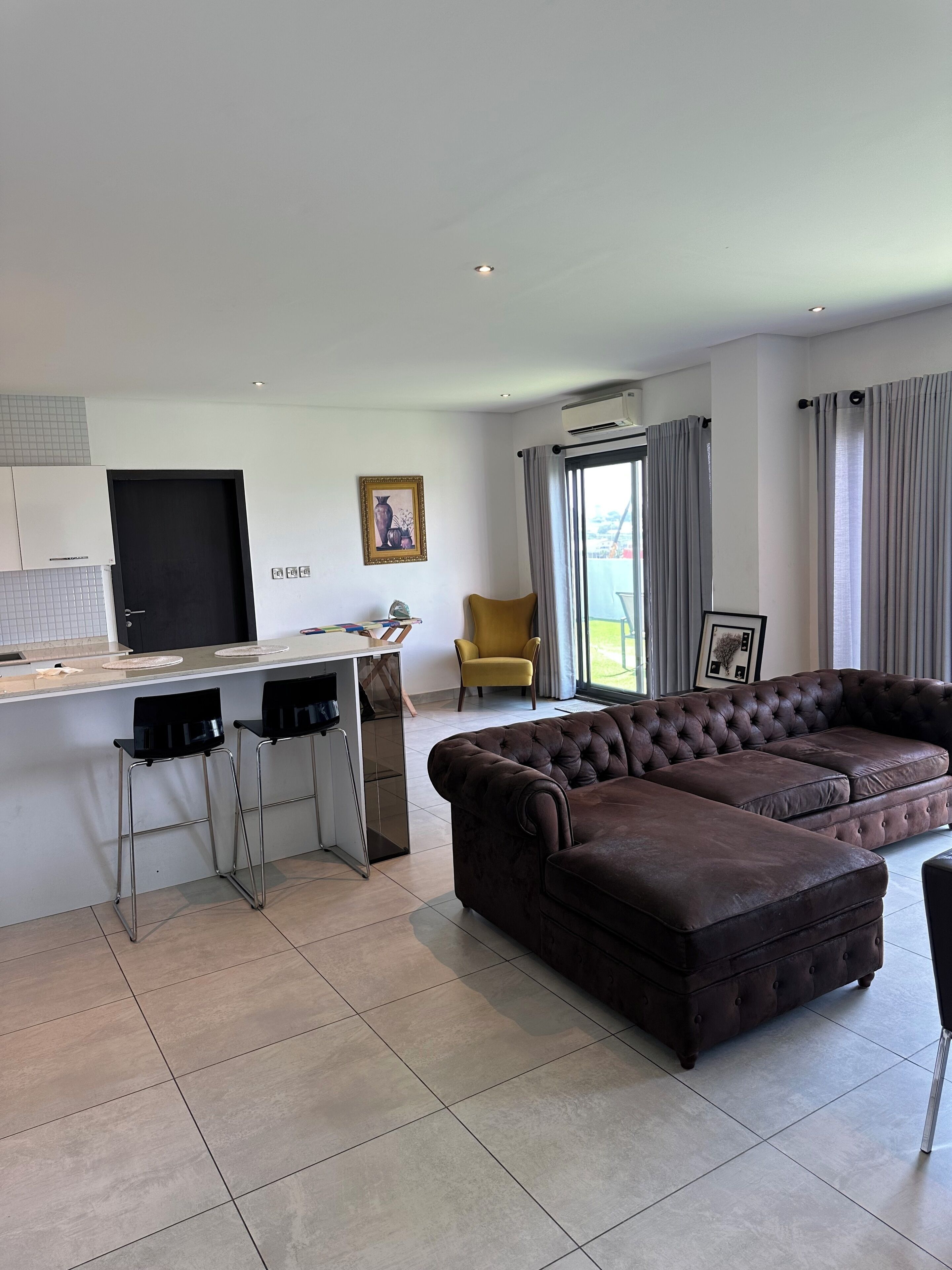 A modern living room with a sectional sofa, a kitchen area with a flat-screen TV, and a dining space with bar stools.
