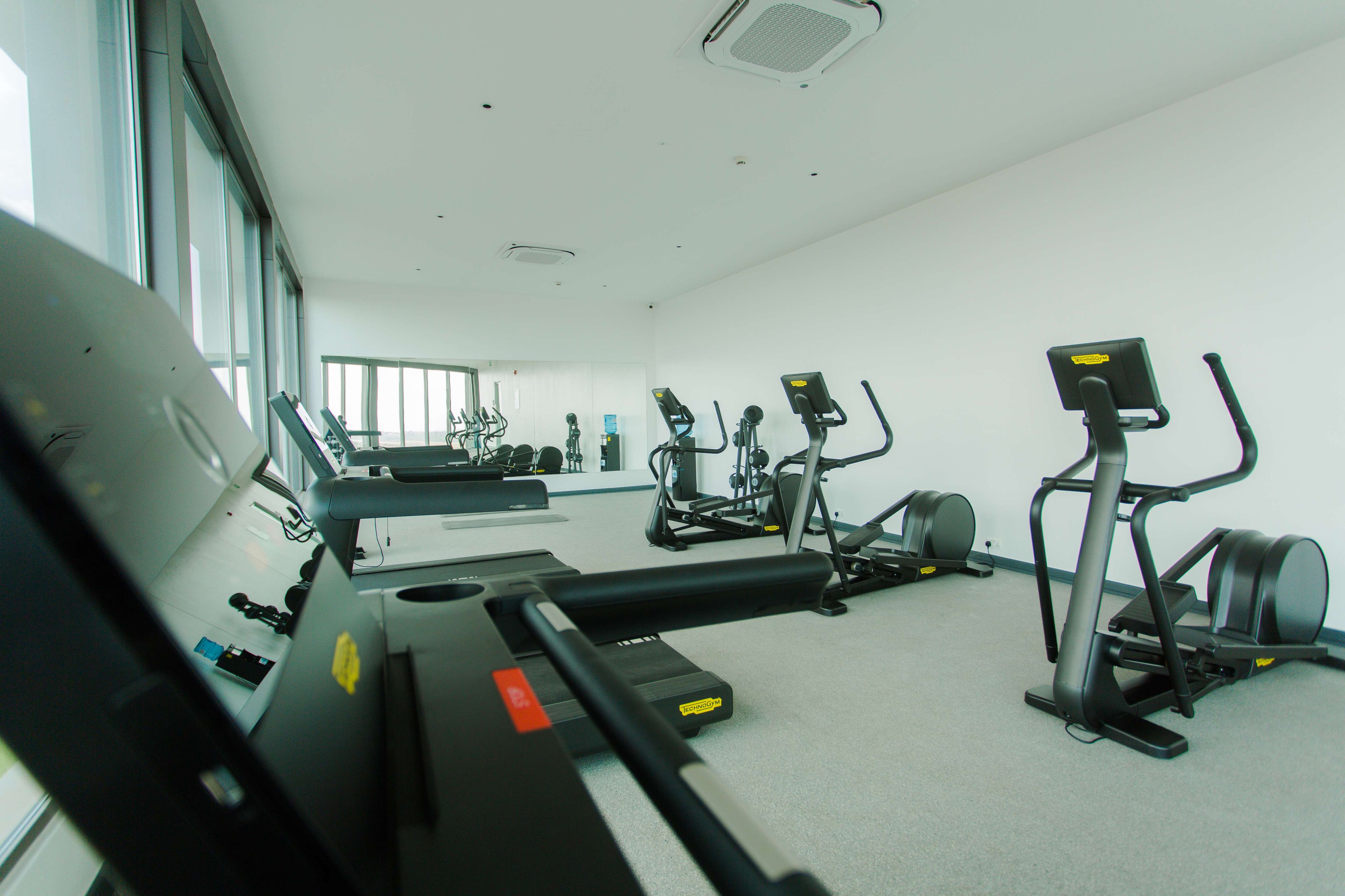 A gym with various exercise equipment, including treadmills and stationary bikes, arranged in a spacious room with large windows.