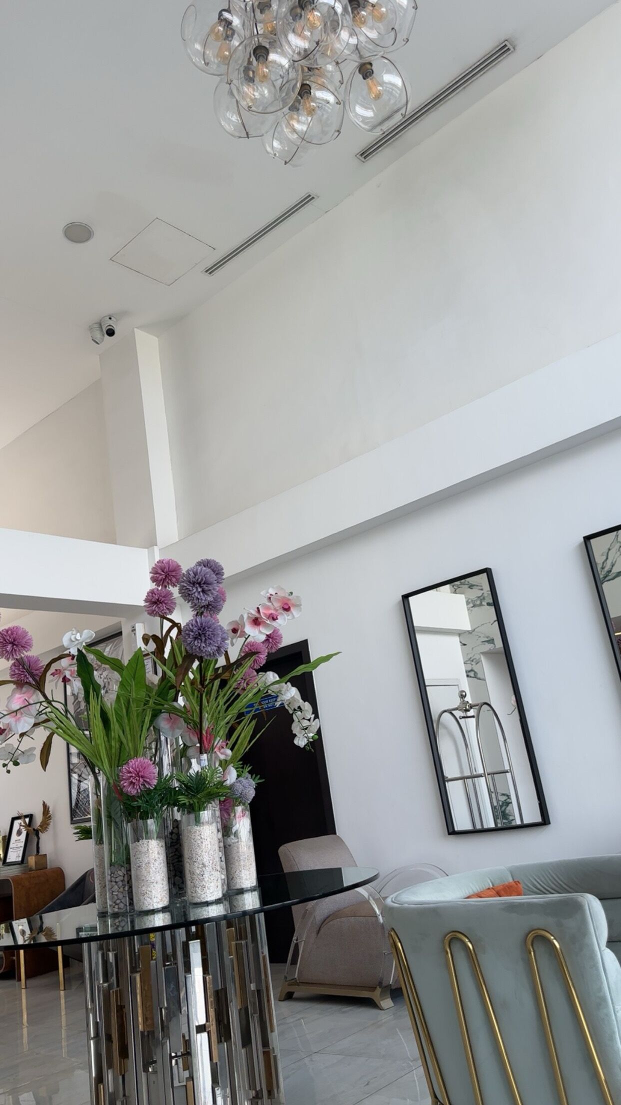 A modern interior with a dining area, a large mirror, and decorative orchids.