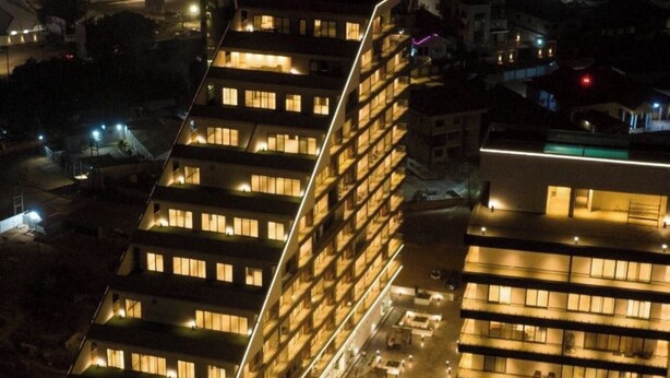 Un hotel moderno con varios pisos, una piscina en la azotea y una fachada bien iluminada.