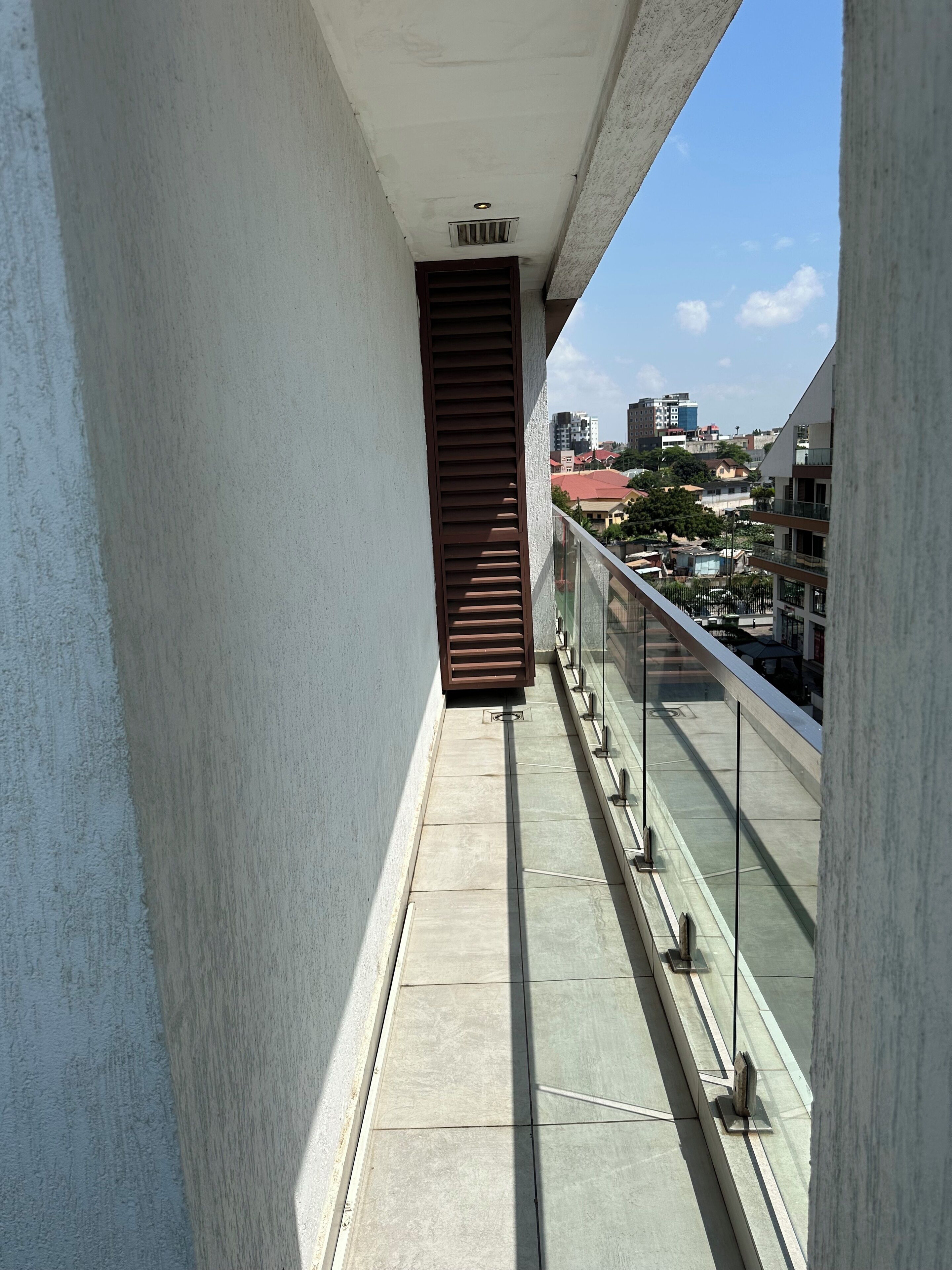 Ein schmaler Balkon mit Metallgeländer, eine braune Tür und ein freier Blick auf die Stadtlandschaft im Hintergrund.