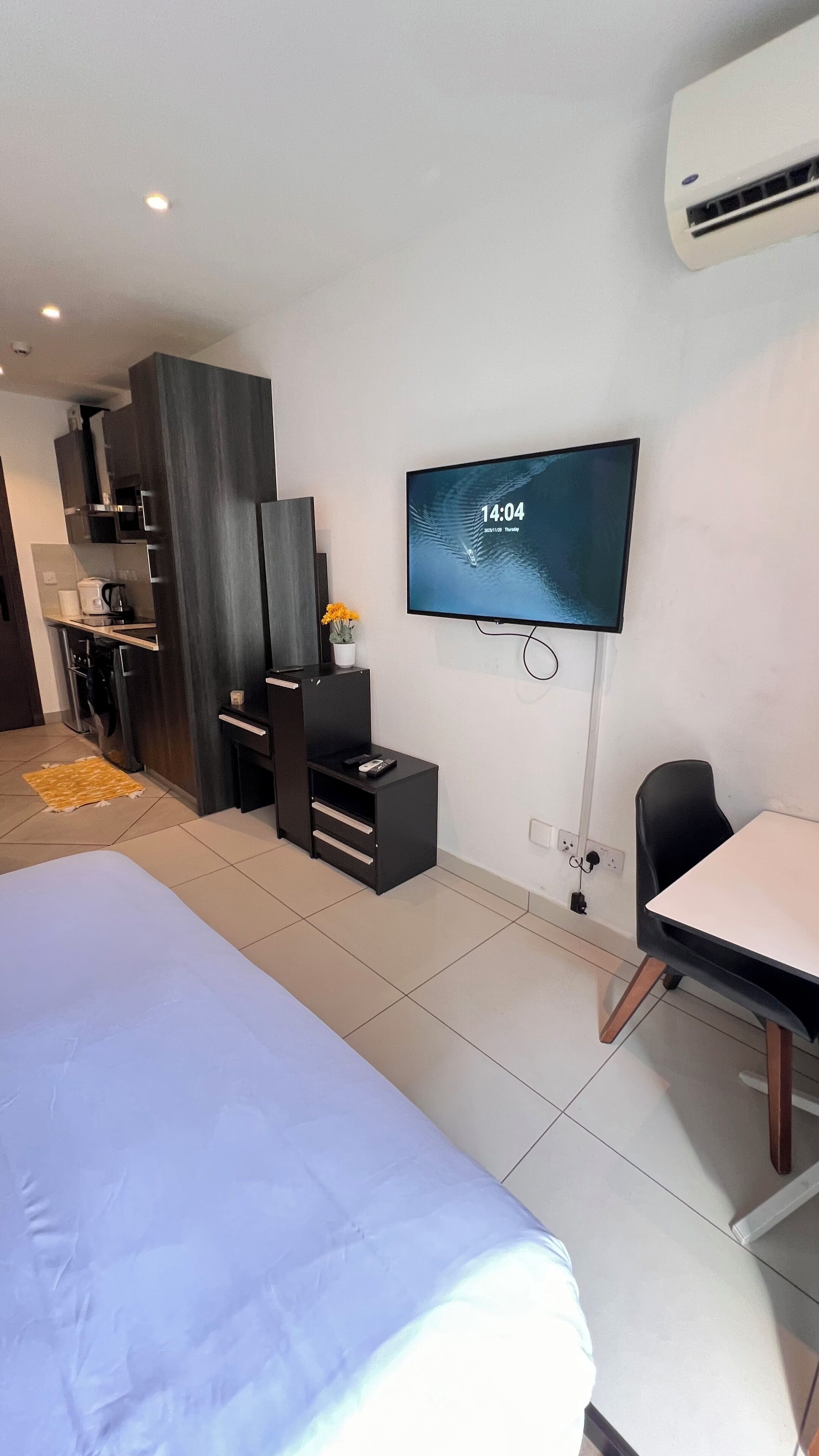 Habitació d'hotel moderna amb un llit gran, un televisor fixat a la paret, un escriptori petit i una zona de cuina equipada.