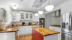 A modern kitchen with white cabinetry, a wooden island, stainless steel appliances, and pendant lighting. - Rooster Row Cottage w/ Pool, Jacuzzi, Fire Pit + Poker Room. Sleeps 12! (West Columbia)