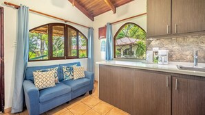 Una cucina accogliente con un divano blu, mobili in legno e ampie finestre da cui si vede il verde.