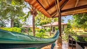 Un'amaca sotto un pergolato in legno, un patio piastrellato e vista su una zona residenziale con case e vegetazione.