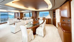Interior lujoso de un yate con una mesa de comedor redonda, asientos blancos tapizados y vista al mar.