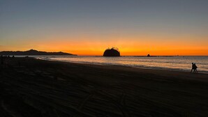 En strand ved solnedgang med en stor klippeformation i det fjerne.