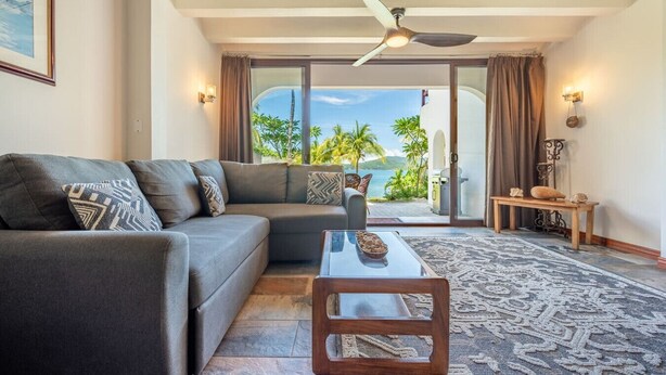 A modern living room with a sofa, a coffee table, and a view of the ocean through large glass doors. - Cultural Charm and Ocean Views in Playa Flamingo (Playa Flamingo)
