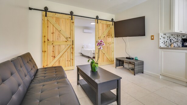 A modern living room with a sofa, a coffee table, and a sliding barn door. - Steps to Pompano Beach: Couple's Retreat w/ Patio! (Pompano Beach)