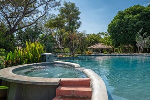 A swimming pool with a hot tub, surrounded by lush greenery and a small building with a tiled roof. - Casa Sereneness Potrero Retreat with Shared Pool (Potrero)