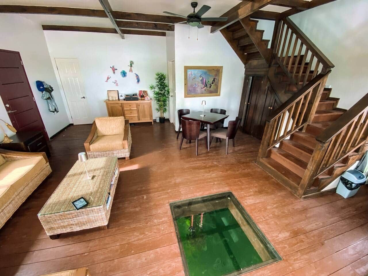 A spacious living area with a wooden floor, a dining table, and a staircase.