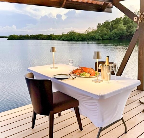 A dining table set on a wooden deck with a view of a lake and forest.