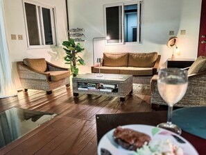 A living room with wicker furniture, a glass coffee table, and a dining table with a plate and a glass.
