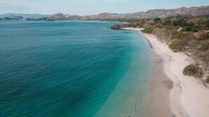 Eine Küstenlandschaft mit klarem türkisblauem Meer, Sandstrand und sanften Hügeln im Hintergrund.