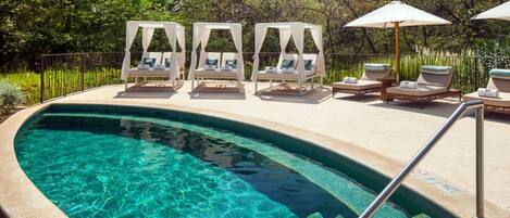 A clear pool with lounge chairs and umbrellas, surrounded by greenery.