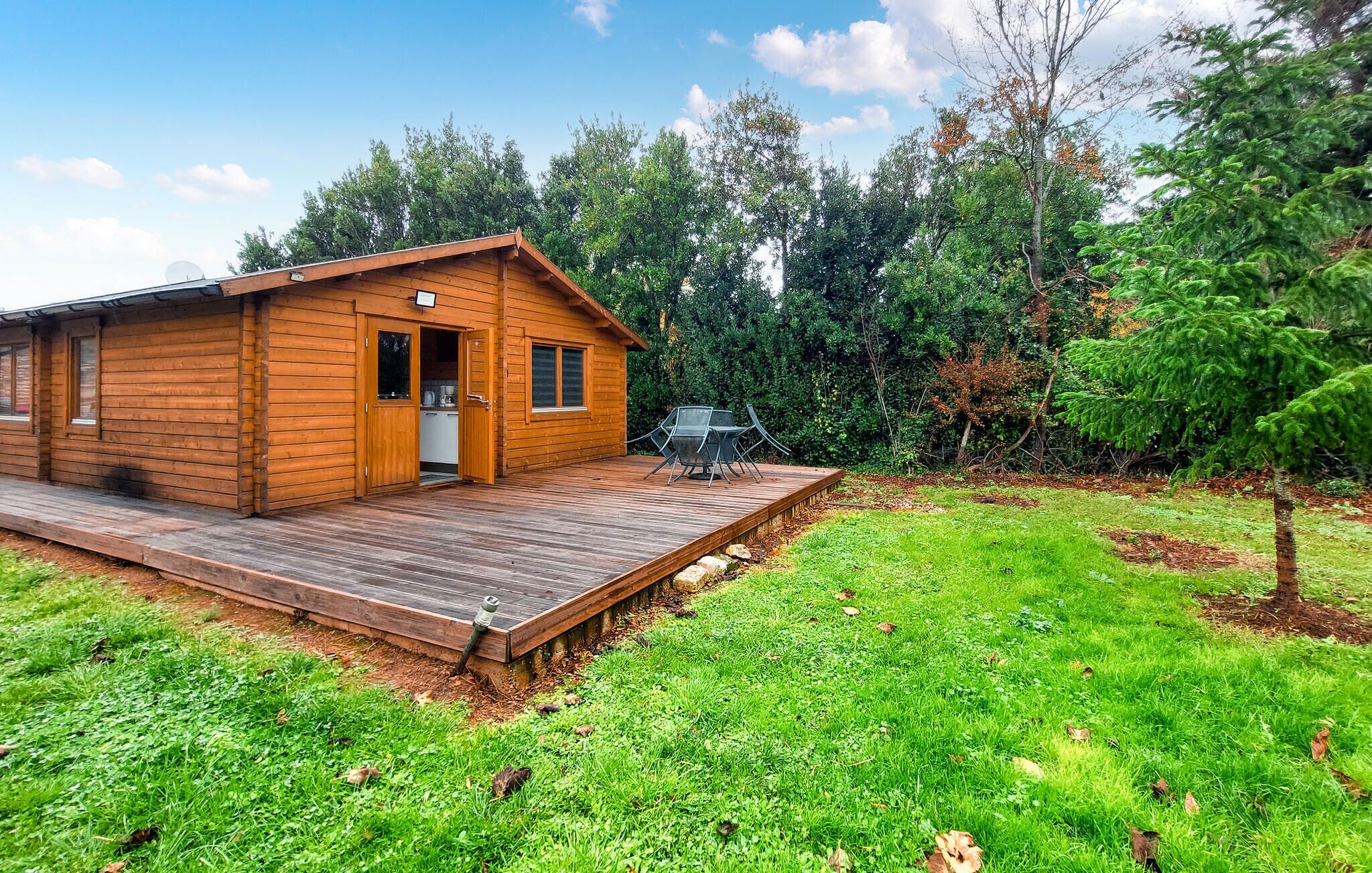 A wooden cabin with a deck, a small kitchen, and a dining area with outdoor furniture.