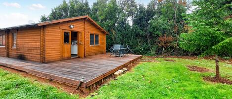 A wooden cabin with a deck, a small kitchen, and a dining area with outdoor furniture.