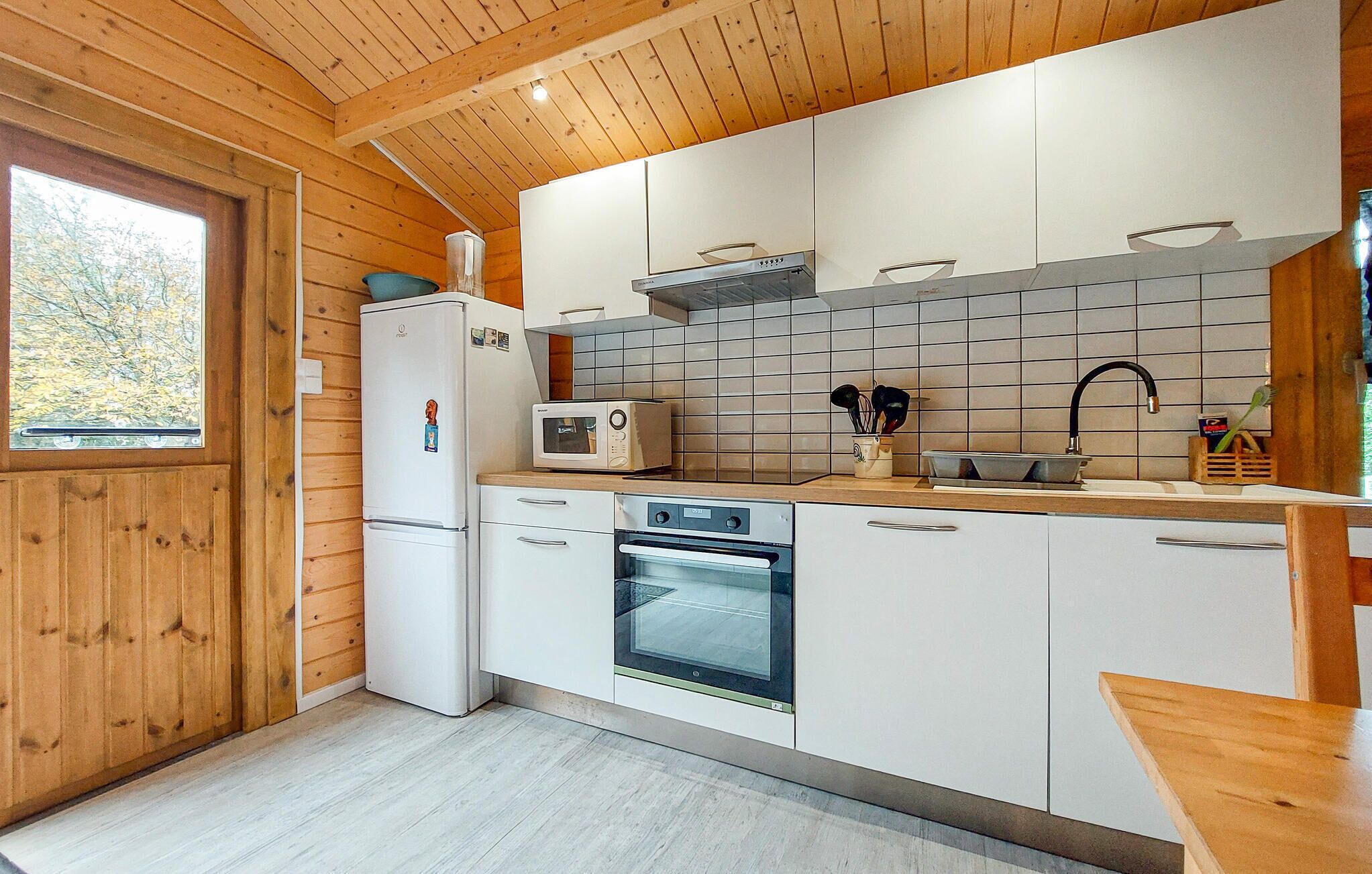 A compact kitchen with wooden walls, a white refrigerator, a microwave, an oven, and a sink with a wooden countertop.