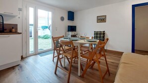 A dining area with a table set for four, wooden chairs, a television, and a door leading outside. - Appartement Proche Plage (Royan)