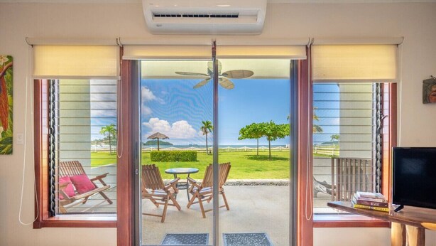 Una habitación con puerta de vidrio corredera que da a un espacio exterior con mesa, sillas y vistas a un paisaje de césped, árboles y una valla.