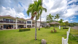 Un hotel con edificios de varios pisos, césped cuidado, palmeras y una valla blanca.