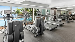 A gym with cardio machines, dumbbells, and a view of a swimming pool.