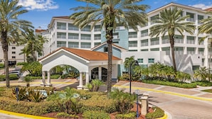 A multi-story hotel with a central courtyard, palm trees, and a swimming pool.