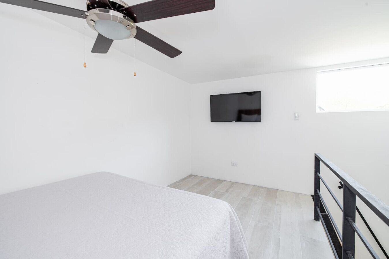 Une chambre à coucher avec un lit, un ventilateur de plafond, un téléviseur fixé au mur et une fenêtre.